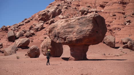 Woman-With-Photo-Camera-Walking-Under-Umbrella-Rock,-Sandstone-Formation-in-Desert-Landscape-of-Arizona-USA