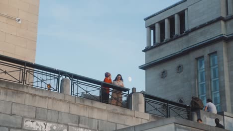 Puesta-De-Sol-En-El-Mont-Des-Arts-En-Bruselas,-Bélgica,-Con-Gente-Caminando-Por-Las-Escaleras-Y-Un-Par-De-Mujeres-Hablando-Casualmente-Y-Con-Caras-Felices-Durante-La-Pandemia