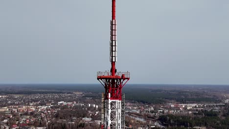 Red-white-communication-TV-tower-rises-up-against-countryside-European-city-Drone-Aerial-View-skyline-background