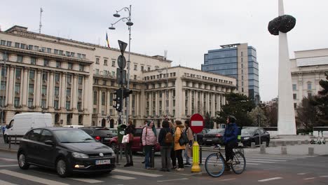 Tráfico-Urbano-Y-Peatones-En-Una-Concurrida-Intersección-En-Bucarest,-Rumania,-Con-Arquitectura-Histórica,-Edificio-Del-Ministerio-Del-Interior.