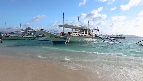 A-pump-boat-is-floating-on-the-clear-turquoise-water-while-being-anchored-on-the-white-sandy-shore-of-an-island-at-El-Nido,-Palawan,-Philippines
