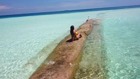 Aéreo,-Disparo-De-Drone,-Alrededor-De-Una-Mujer,-En-Traje-De-Baño-Amarillo,-Sentada-En-La-Arena,-Revelando-Un-Resort-Con-Villas-En-El-Mar-Azul,-En-Un-Día-Soleado,-En-La-Isla-Conrad-Rangoli,-En-Maldivas