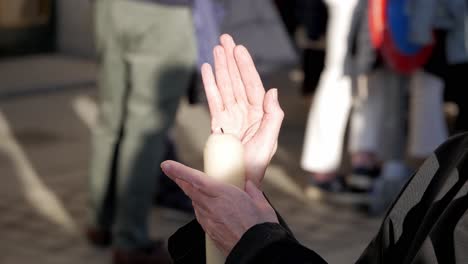 Primer-Plano-De-Un-Cirio-De-Pascua-Sostenido-Y-Protegido-Del-Viento-Con-La-Mano-Durante-Una-Celebración-En-Madrid