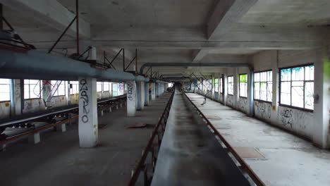 Indoor-drone-shot-tracking-a-conveyor-belt-in-an-old-abandoned-warehouse-factory-covered-in-graffiti