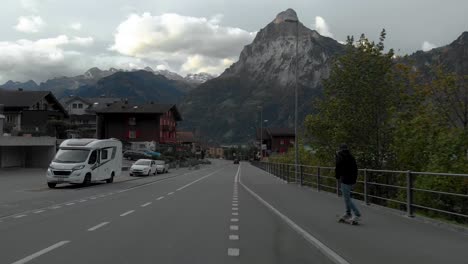 Drone-Aerial-View-of-Skater-on-Road-Junction-Under-Swiss-Alps-Peaks-Near-Lucerne,-Switzerland