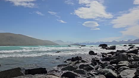 Panoramic-video-of-turquoise-glacial-waves-splashing-on-the-rocks-in-Lake-Tekapo,-Mackenzie-Country,-New-Zealand's-central-South-Island