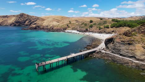 Imágenes-De-Drones-Volando-Hacia-Un-Embarcadero-Que-Sobresale-De-Un-Océano-Azul-Brillante-Con-Dos-Playas-De-Arena-Blanca-Cercanas-Separadas-Por-Una-Enorme-Formación-Rocosa