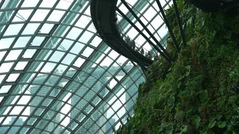 A-tilt-down-shot-capturing-people-walking-on-the-aerial-walkway,-with-views-of-Marina-Bay-Sands-through-the-glass-windows-of-the-Cloud-Forest-Conservatory,-Gardens-by-the-bay,-Singapore