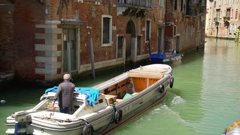 Slow-motion-shot-of-Italian-man-navigating-his-motorboat-through-the-canal-of-Venice