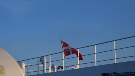 Danish-national-flag-fluttering-hung-on-a-metal-mast-on-the-upper-deck-of-a-ferry,-beautiful-sunny-evening