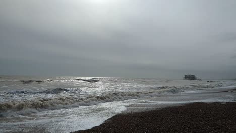 Amplia-Vista-De-La-Playa-De-Brighton-Con-El-Muelle-Oeste-Abandonado-Y-El-Sol-Brumoso-En-Un-Día-Nublado