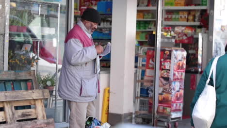 Un-Anciano-Completa-Un-Crucigrama-Mientras-Espera-Afuera-De-Una-Tienda-En-Londres,-Inglaterra