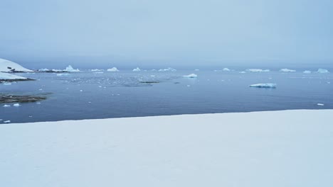 Snowy-Winter-Landscape-with-Icebergs-in-Antarctica,-Snow-and-Iceberg-Scenery-in-Antarctic-Peninsula-Looking-Out-to-Ocean-Sea-Water-from-Mainland-Antarctica-Land