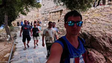 Athens,-Greece:-Slow-motion-of-a-tourist-couple-visiting-Acropolis-of-Athens,-Greece,-in-front-of-the-remains-of-the-famous-Parthenon-on-a-windy-day