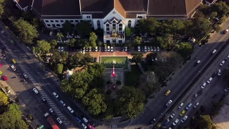 Thai-flag-blowing-in-front-of-Customs-Department-near-busy-road,-aerial-top-shot