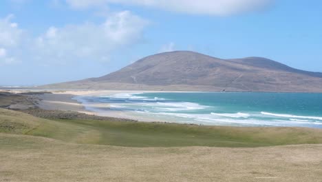 Wunderschöner-Malerischer-Blick-Auf-Das-Blaue-Meer-Mit-Wellen,-Die-An-Den-Strand-Rollen,-Und-Die-Raue,-Wilde-Und-Bergige-Landschaft-Auf-Den-Inseln-Lewis-Und-Harris-Auf-Den-Äußeren-Hebriden-Im-Westen-Schottlands,-Großbritannien