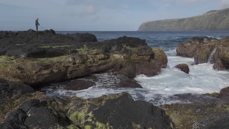 Person-exploring-rocky-coastline-in-Mosteiros,-Sao-Miguel,-dramatic-waves-crashing-on-black-volcanic-rocks,-daylight
