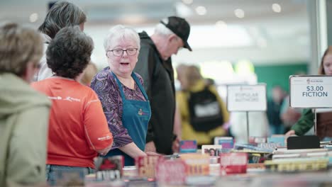 Una-Mujer-Mayor-Exhala-Sorprendida-Y-Parece-Abrumada-Ante-Una-Venta-De-Libros-Usados-En-Un-Centro-Comercial.