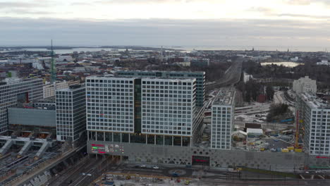 Aerial,-rising,-drone-shot-tilting-towards-the-Mall-of-Tripla-shopping-center-and-the-Pasila-railway-station,-on-a-partly-sunny-evening,-in-Helsinki,-Finland