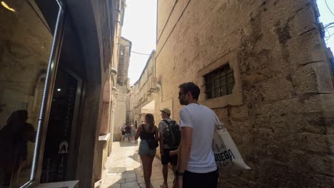 Tourist-strolling-narrow-alleyways-of-Dubrovnik-Old-City,-People-walking-past-Game-Of-Thrones-fan-shop