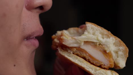 Eating-a-sliced-chicken-burger,-close-up-mouth-and-face-shot,-studio-background