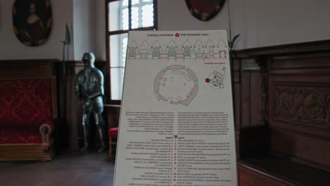Informative-display-about-Trakoscan-Castle's-Chivalric-Hall,-featuring-a-suit-of-armor-and-historical-interiors