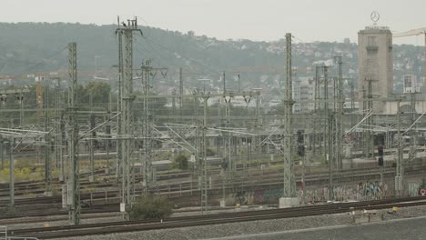 Busy-European-railway-station-with-multiple-trains,-overhead-lines,-and-urban-backdrop