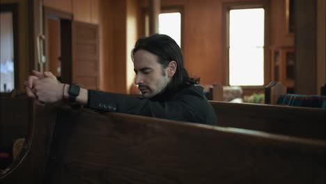 Young-man-in-black-suit-praying-in-church-pew-in-cinematic-slow-motion-with-folded-hands