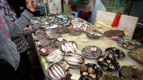 Gente-Haciendo-Trueques-En-El-Mercado-De-Pescado-Frente-A-Una-Mesa-Con-Un-Montón-De-Pescados-Diferentes-En-Exhibición