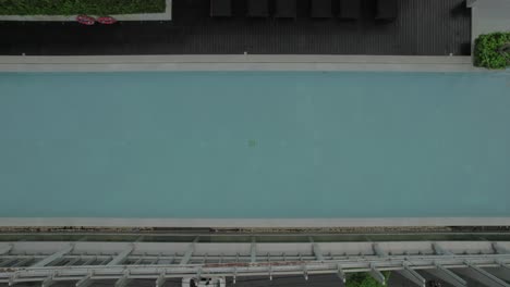 Aerial-view-of-a-rooftop-swimming-pool-with-lounge-chairs-and-greenery,-situated-above-a-city-street-with-cars