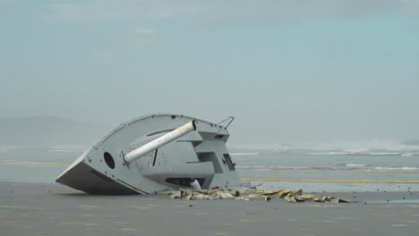 Waves-Rushing-Past-Washed-Up-Yacht-on-Gloomy-Beach---Wide-Static-Shot