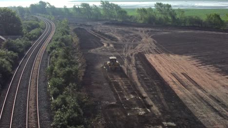 Aerial-view-circling-bulldozer-leaving-housing-construction-site-next-to-railway-tracks-in-the-early-morning-sunrise