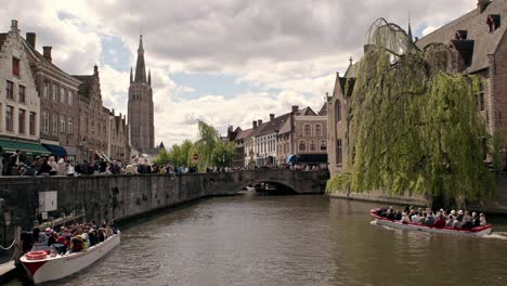 Boat-Tours-On-Sint-Janskaai-In-Bruges,-Belgium-With-View-Of-Tower-of-the-Church-of-Our-Lady