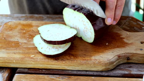 Cutting-eggplant-with-sharp-knife-on-wooden-chopping-board,-closeup