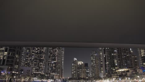 Night-cruise-along-Dubai-Marina-canal,-passing-under-overhead-bridge