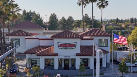 Temecula-Krispy-Kreme-Drone-Vuela-Hacia-El-Frente-Del-Edificio-Pasando-árboles-Y-El-Brazo-De-La-Luz-De-La-Calle