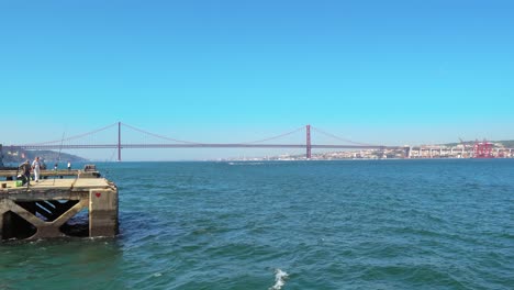 Fischer-Fischen-Auf-Betonplattformen-Auf-Dem-Tejo-Mit-Der-Skyline-Von-Lissabon-Und-Der-Brücke-Ponte-25-De-Abril-Im-Hintergrund-An-Einem-Sonnigen-Tag-In-Portugal