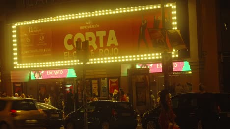 Busy-city-theater-in-Barcelona-during-night-time,-illuminted-street-full-of-people-and-cars-driving-road-