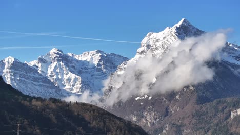 Hermosa-Vista-De-Montañas-Nevadas-Con-Nubes-Volando-Hacia-La-Tierra-Con-Un-Cielo-Azul-Soleado-En-Glarus,-Suiza