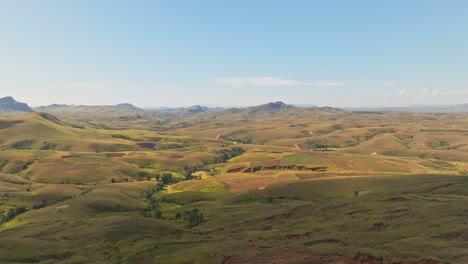 Aerial-view-of-beautiful-Madagascar-countryside-with-soil-erosion,-green-fields-and-mountains-on-sunny-day