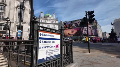 Piccadilly-Circus-Station-Informationsschild-Zeigen,-Welche-Linien-Verfügbar-Sind,-Da-Verkehr-Und-Menschen-An-Sonnigen-Morgen-Vorbeigehen