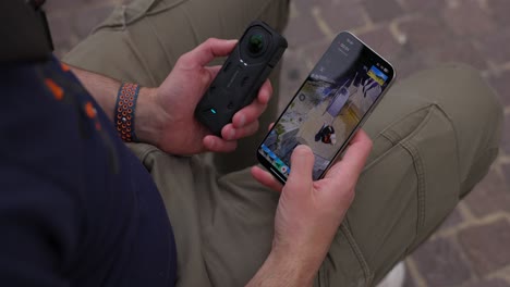 Man-holds-360-camera-in-hand-while-scrolling-to-view-video-clip-on-smartphone