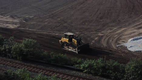 Bulldozer-moving-earth-creating-foundation-road-alongside-railroad-aerial-dolly-view-on-early-morning-sunrise-construction-site