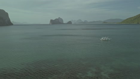Barco-Catamarán-En-Aguas-Tropicales-Por-Islas-Acantiladas-En-Filipinas,-Extracción-Aérea
