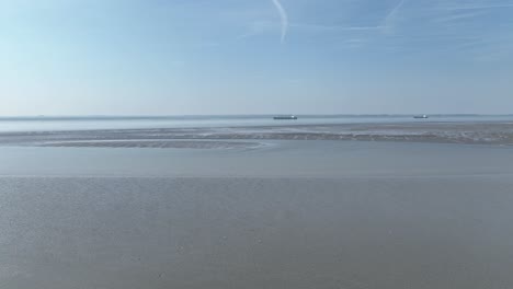 Flying-over-the-sea-in-low-tide-with-tankers-in-the-background