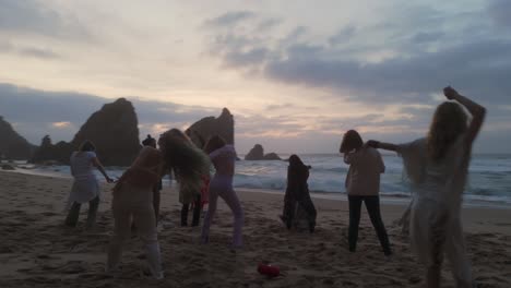 Mujeres-Felices-Bailando-En-La-Playa-Con-Grandes-Acantilados-En-Segundo-Plano.