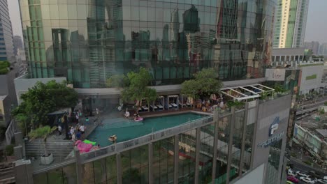 Urban-reflection-on-glass-building-with-rooftop-pool-in-Bangkok---aerial