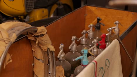 Close-up-of-antique-bottles-in-box-near-vintage-motorcycle-in-museum