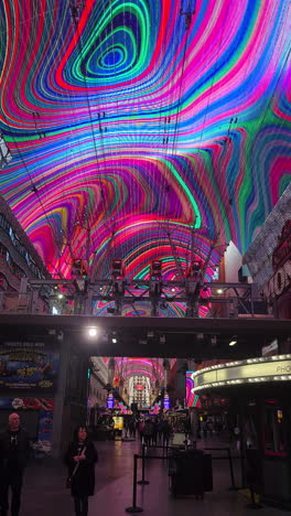 Vertical-Video,-Fremont-Street-Experience,-Downtown-Las-Vegas-Nevada-USA,-People-Walking-Under-Flashy-Ceiling-Colors