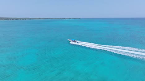 Small-boat-drives-on-crystal-clear-blue-water-to-exotic-island,-aerial-orbit